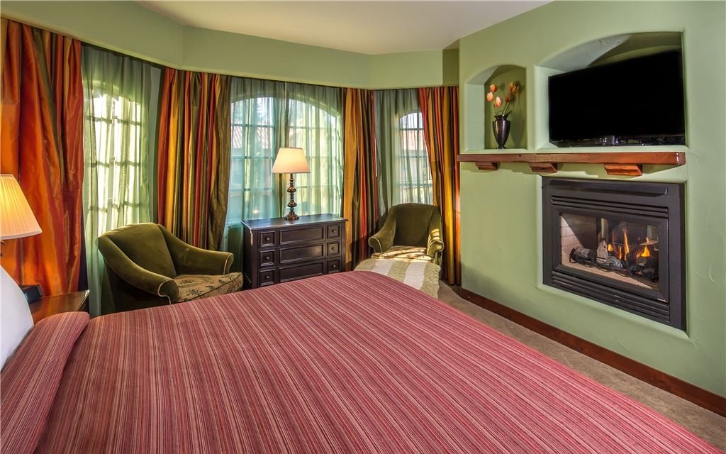 Bedroom with fireplace, armchairs, a television, and large curtained windows