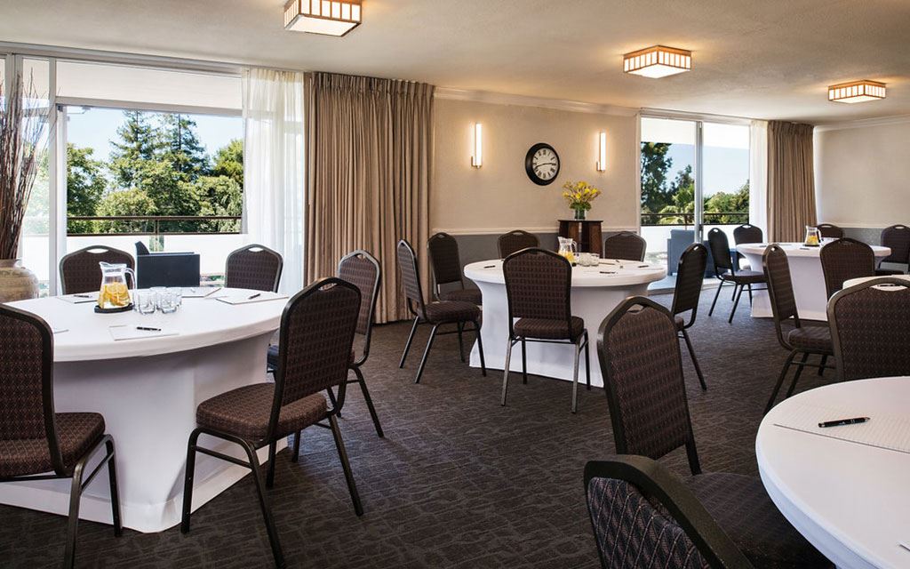 White-clothed tables surrounded by chairs in a windowed dining space